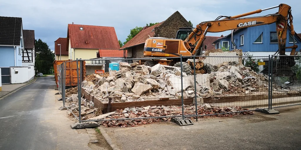 Baustelle nach Teilabbruch mit Bauzaun und Bagger